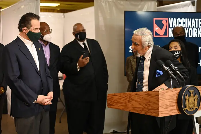 Governor Cuomo, in a suit wearing a mask, stands as Charles Rangel, in a suit, look at him during a press conference